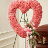 Pink heart-shaped floral wreath on an easel beside a casket