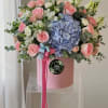 Pink roses and blue hydrangea in a pink hatbox with ribbon