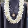 A dense, white double orchid lei draped over a dark graduation gown