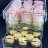 Pink roses in a clear box above gold-wrapped chocolates.