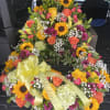 Bright heart-shaped funeral wreath with sunflowers, roses, and a yellow ribbon