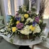 Basket arrangement of yellow roses, white hydrangeas, and purple flowers