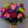 Pink roses and purple flowers arranged in a glass vase with burlap wrap