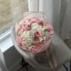 Pink and white bouquet of roses, hydrangeas, and carnations wrapped in pale pink paper