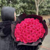 Person holding a large bouquet of bright pink roses wrapped in black paper