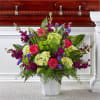 Tall arrangement of pink roses, green hydrangeas, and purple flowers in a white container