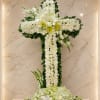 White floral cross arrangement with lilies and roses on a marble wall