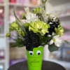 Bouquet of green, white, and black flowers in a bright green cup with eyes