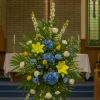 Tall floral spray with blue, yellow, and white flowers in a church