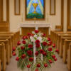 Red rose standing spray with white ribbon in a church aisle