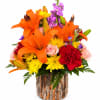 Orange lilies, yellow mums, pink roses, and red carnations in a bark-covered container