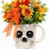 Orange and yellow flowers arranged in a skull-shaped mug with a ribbon