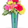 Pink lilies, gerbera daisies, and yellow carnations in a blue-green vase