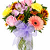Mixed bouquet of pink roses, gerbera daisies, and carnations in a glass vase with a purple bow