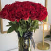 A tall vase of red roses tied with a black ribbon