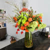 Orange roses and green blooms in a tall glass vase