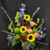 Tall mixed arrangement with sunflowers, orange roses, purple blooms, and blue flowers in a metal vase.