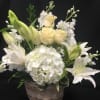 White lilies and pale roses in a woven basket with a large white hydrangea bloom