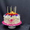 Round floral cake with white, red, yellow, and blue flowers and tall candles