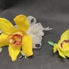 Two yellow orchid corsages with ribbon and greenery on a dark background