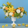 Yellow and white flower arrangement in a white pedestal vase with lemons
