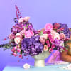 Pink and purple floral arrangement in a pedestal vase with roses and hydrangeas