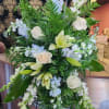 Standing floral spray with white roses, lilies, and pale blue blooms