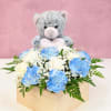 Blue and white carnations in a wooden box with a teddy bear