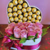 Heart-shaped box of gold-wrapped chocolates with pink roses in front