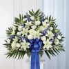 White lilies and blue flowers in a standing arrangement with a blue ribbon