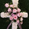 Pink roses and white flowers arranged on a cross with a lavender ribbon