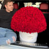 Man sitting beside a large red rose arrangement in a white hatbox