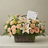 Peach roses and lilies arranged in a wicker basket with a note card