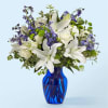 White lilies and purple flowers in a blue glass vase