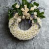 White floral wreath with cream roses and purple accents on a stand