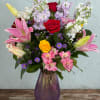 Mixed bouquet of roses, lilies, and purple flowers in a purple vase