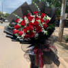 Large bouquet of red roses with white filler flowers wrapped in black paper