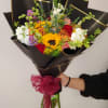 Mixed bouquet with a sunflower, roses, and white blooms wrapped in black paper