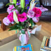 Bouquet of pink roses, purple lilies, and blue delphinium in a glass vase