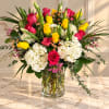 Bouquet of pink and yellow roses with white hydrangeas in a clear glass vase