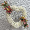 Heart-shaped white floral wreath with pink rose accents on a stand