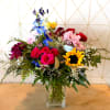 Mixed bouquet with roses, sunflowers, and blue flowers in a glass vase