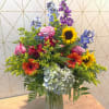 Mixed bouquet in a glass vase with roses, sunflowers, hydrangea, and blue-purple blooms