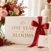 Gift box with a red ribbon beside rose bouquets and a card