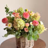 Mixed floral arrangement in a woven basket with pink, peach, white, and green blooms