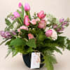 Pink tulips and roses arranged in a black pot with greenery