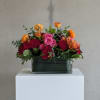 Mixed bouquet of red, pink, and orange flowers in a rectangular glass vase