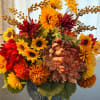 Silk arrangement of orange, yellow, and red mums and sunflowers in a blue ceramic pot.
