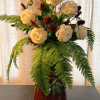Tall arrangement of cream blooms with red accents and cascading fern fronds in a red ceramic vase