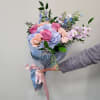 Handheld bouquet of pink roses and pastel blue flowers wrapped in blue paper